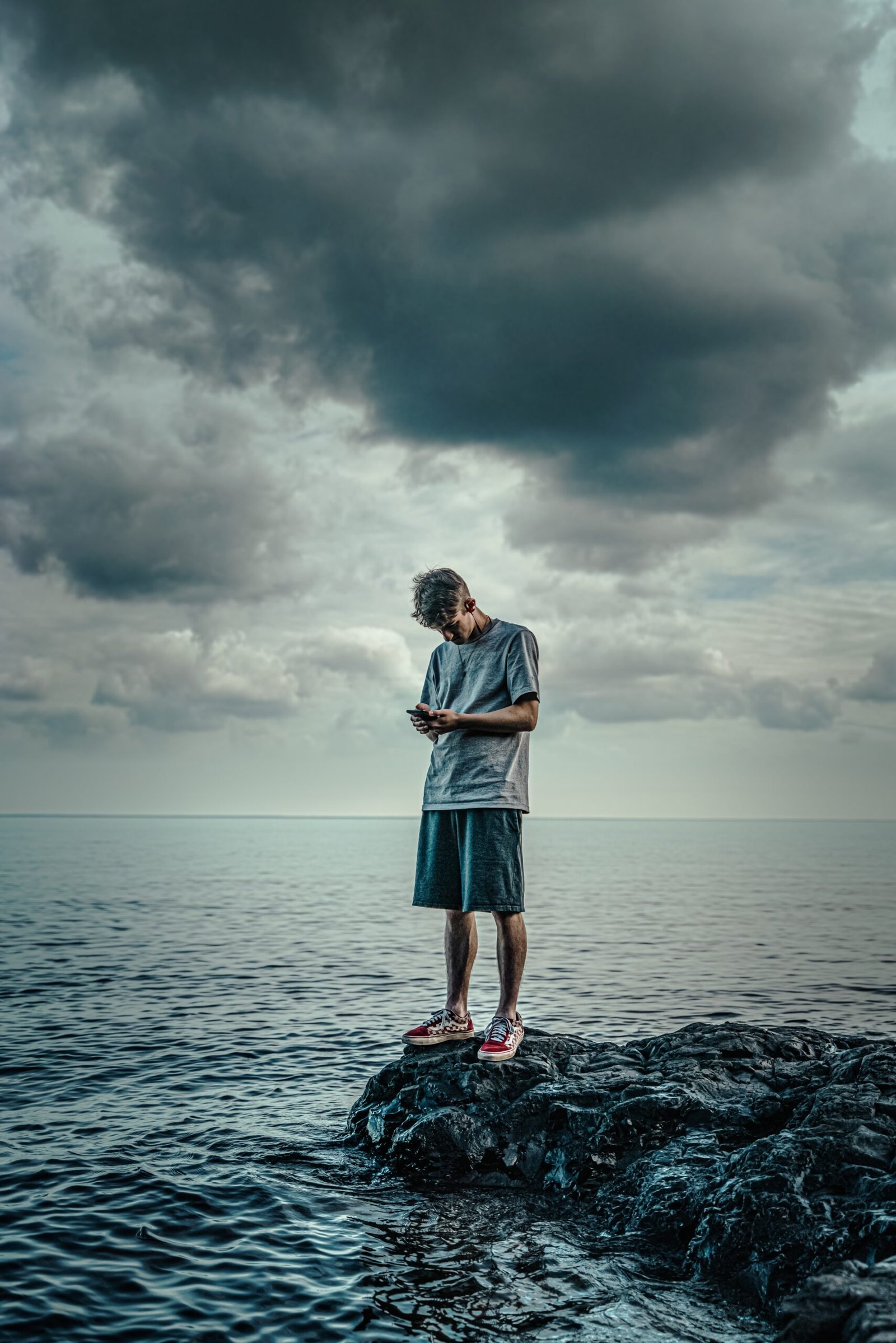 woman in white long sleeve shirt and blue skirt standing on rock in front of sea